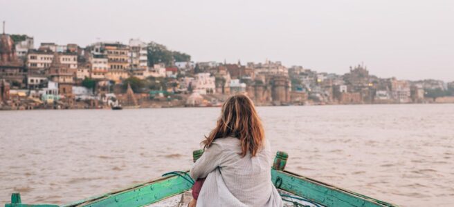Woman sitting on a boat enjoying the tranquil view of Varanasi cityscape.