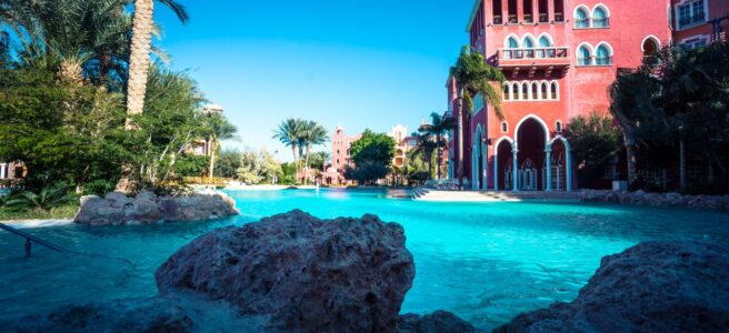 Stunning resort poolside area with palm trees and vibrant red architecture on a sunny day.
